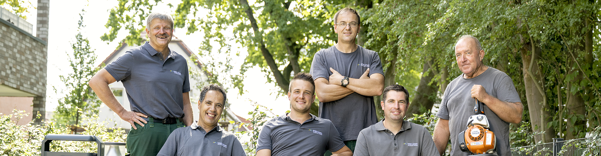 Gruppenfoto: Unser Gartenpflege-Team sitzt auf einer Bank vor unserem Wohngebäude. Alle Personen lächeln in die Kamera.