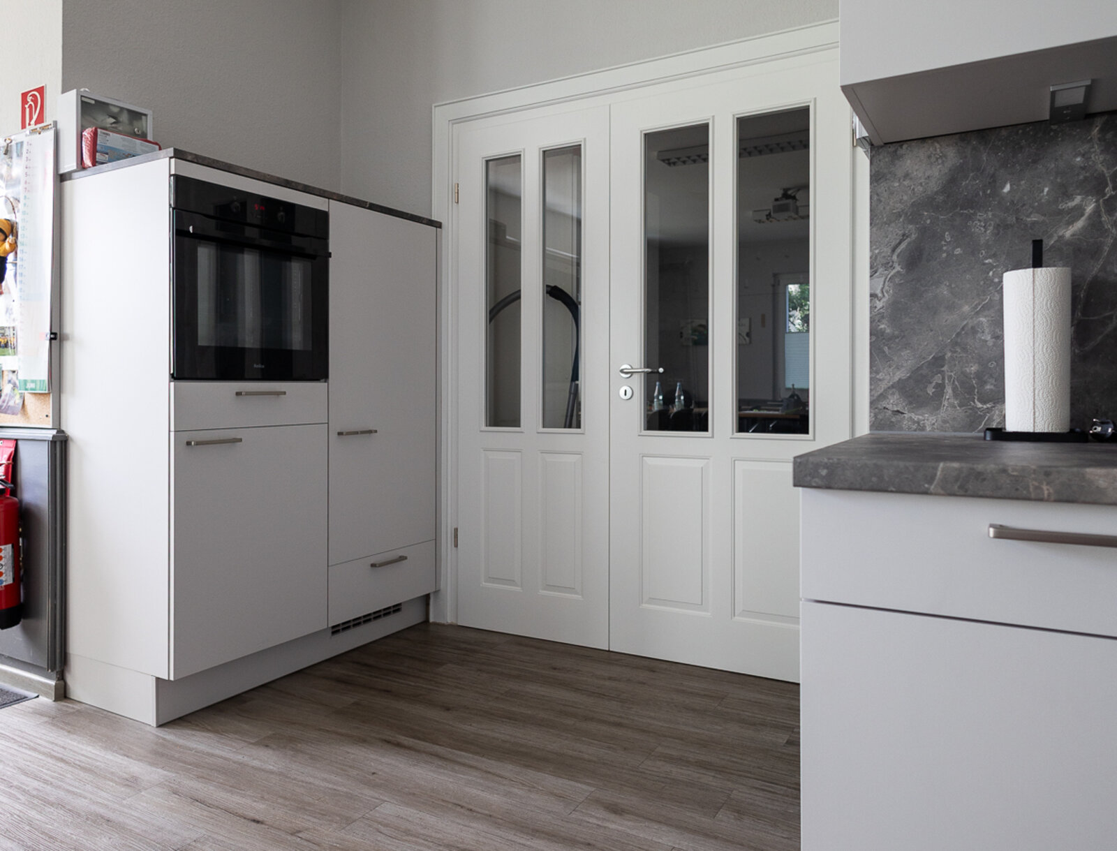 Moderne Einbauküche im Gemeinschaftsraum in Lünen-Horstmar mit Backofen, Hochschrank und weißer Tür.