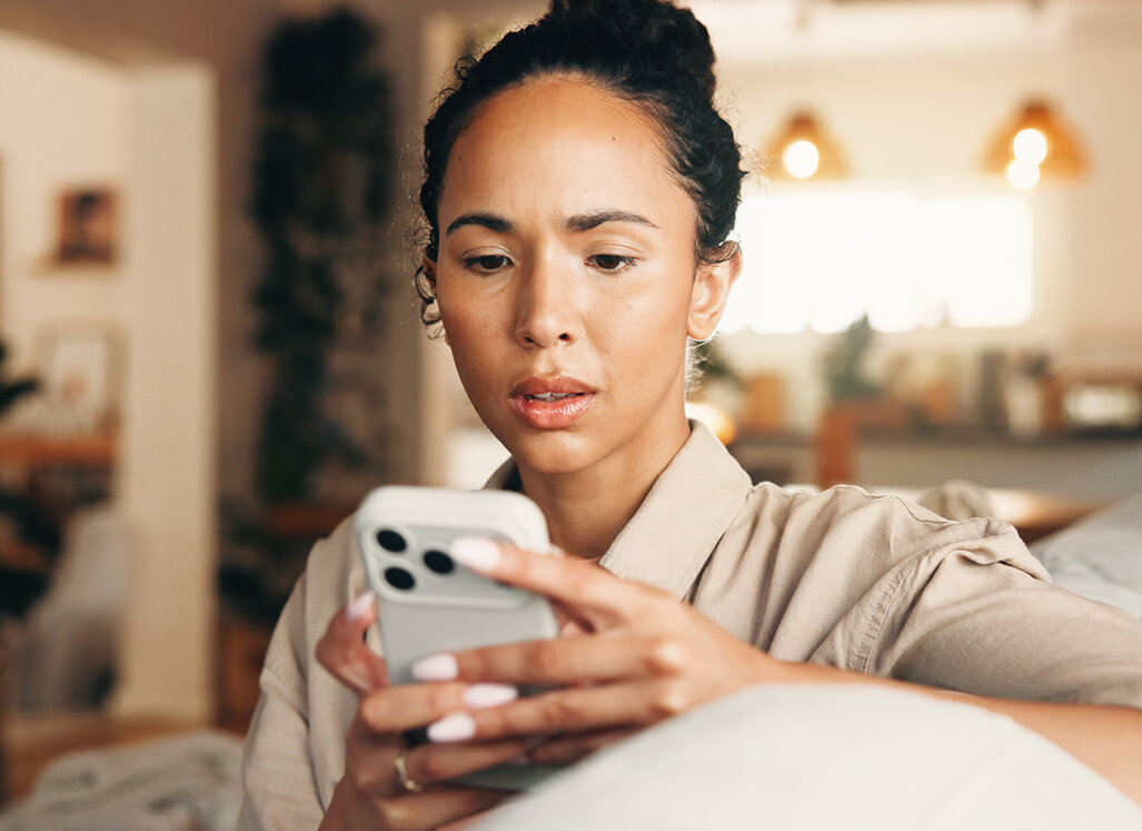 Junge Frau schaut besorgt auf ihr Smartphone. Das Bild steht im Zusammenhang mit Telefonbetrug und der Sensibilisierung für Betrugsmaschen.