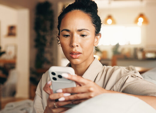 Junge Frau schaut besorgt auf ihr Smartphone. Das Bild steht im Zusammenhang mit Telefonbetrug und der Sensibilisierung für Betrugsmaschen.