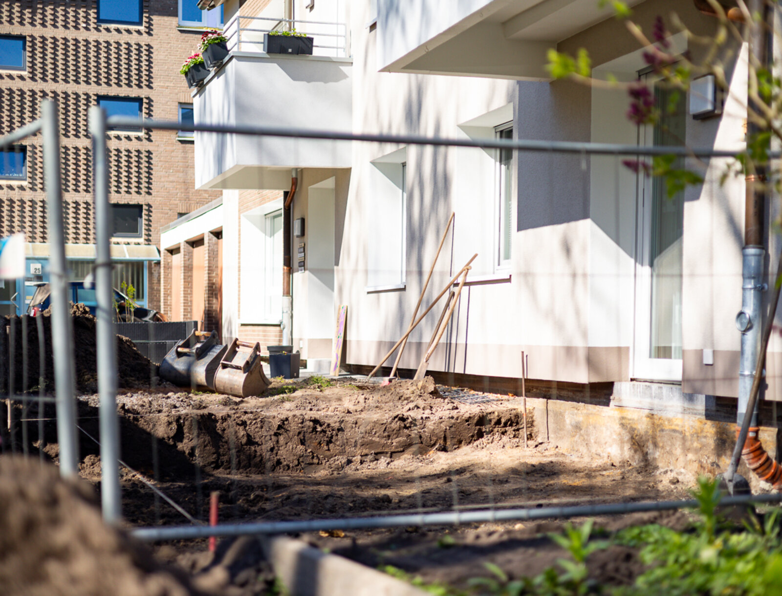 Außenanlagen eines modernisierten Mehrfamilienhauses während der Neugestaltung. Bauarbeiten mit Erdarbeiten und Werkzeugen im Vordergrund.