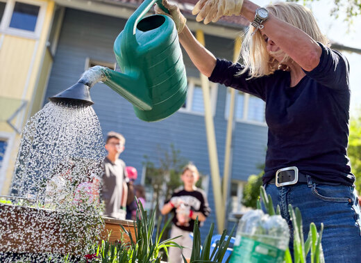Simone Spitzer (WBG Lünen) gießt mit einer Gießkanne Pflanzen in einem Hochbeet, Kinder stehen im Hintergrund.