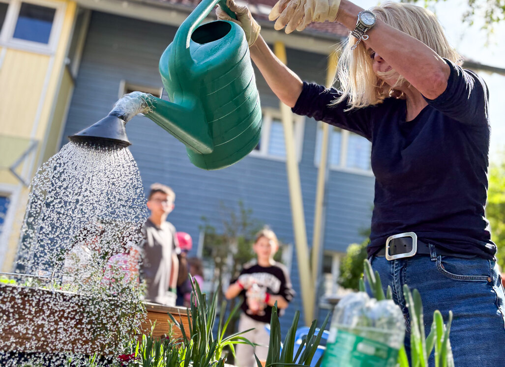 Simone Spitzer (WBG Lünen) gießt mit einer Gießkanne Pflanzen in einem Hochbeet, Kinder stehen im Hintergrund.