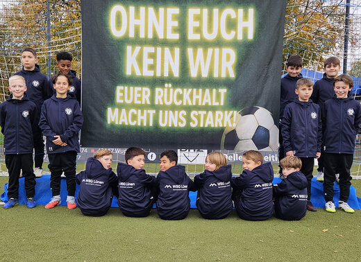 Gruppenfoto des Fußballteams: Kinder schauen lächelnd in die Kamera und halten das Banner in die Luft