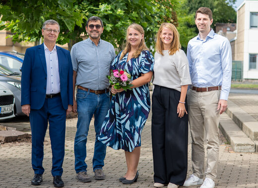 Gruppenfoto: Die Personen stehen gemeinsam vor der Verwaltung und lächeln in die Kamera.