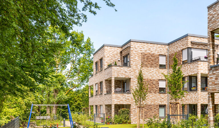 Claudia Dreysse Modernes Wohngebäude der WBG Lünen mit heller Klinkerfassade und mehreren Balkonen, umgeben von Bäumen und Grünflächen.