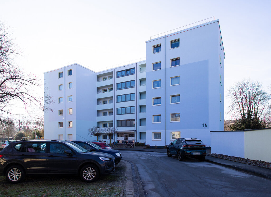 Modernisiertes Mehrfamilienhaus mit hellblauer Fassade und parkenden Autos im Vordergrund.