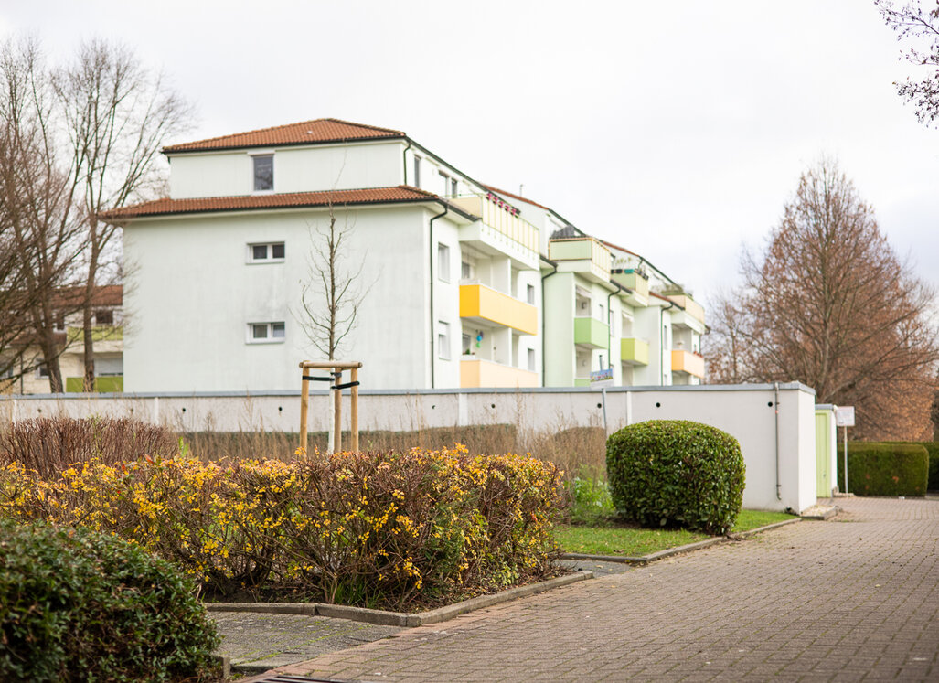 Wohngebäude in einer Wohnanlage in Lünen-Horstmar mit hellen Fassaden und farbigen Balkonen. Im Vordergrund sind gepflegte Grünflächen, Sträucher und ein gepflasterter Weg zu sehen.
