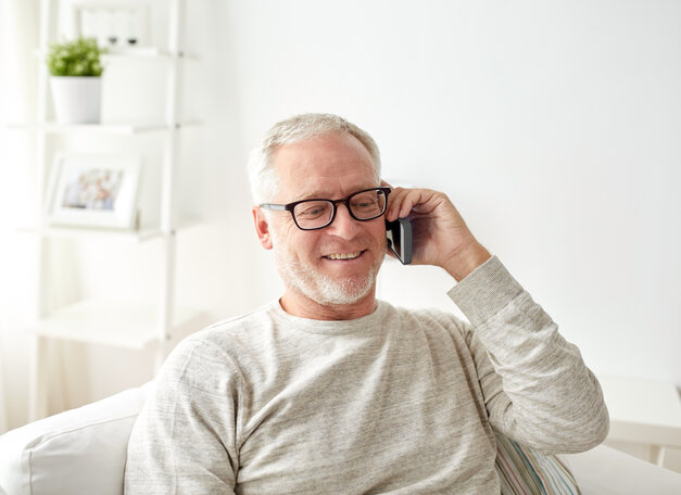Männliche Person mittleren Alters sitzt auf dem Sofa und telefoniert. Sie hat einen freundlichen Gesichtsausdruck.