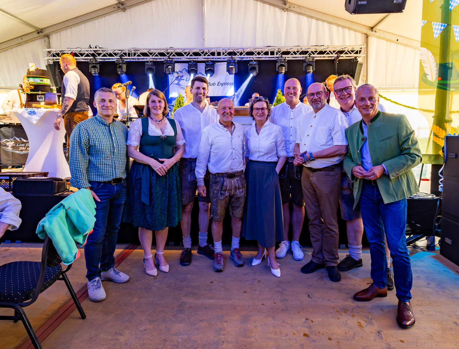 Neun Gäste stehen gemeinsam für ein Gruppenfoto vor der Bühne des Bayerischen Abends.