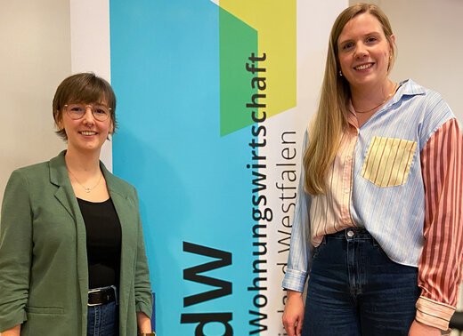 Jana Neumann und Kristina Klee vor einem Roll-Up des VdW. Sie lächeln beide in die Kamera.