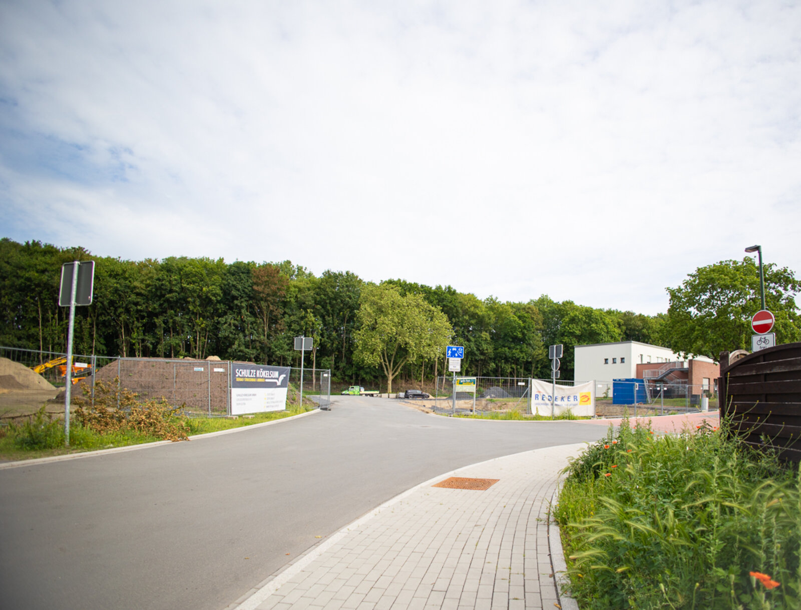 Erschließungsstraße und Gehweg führen zu dem eingezäunten Neubaugebiet am Herbert-Eppen-Weg.
