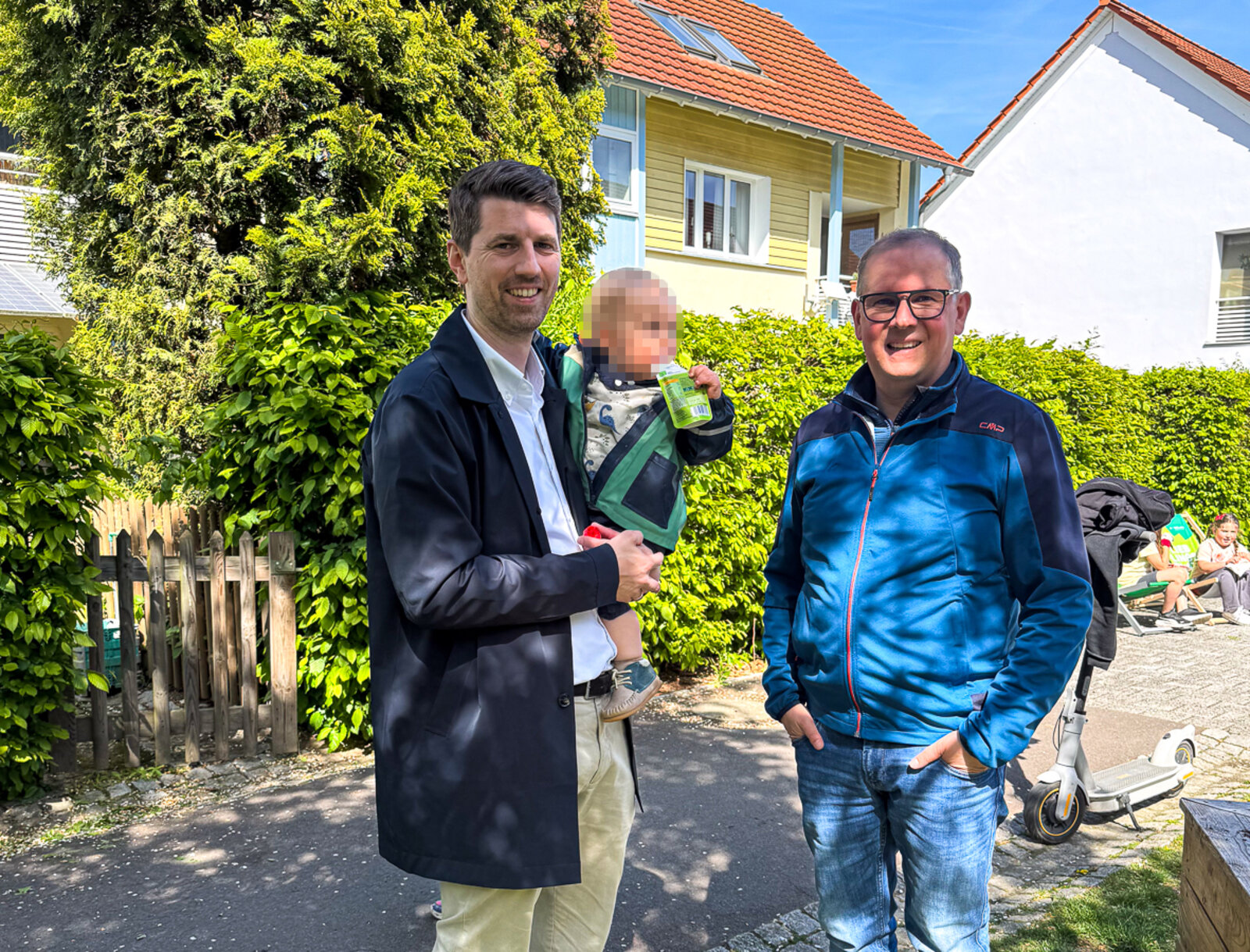 Vorstand Jan Hische hält seinen kleinen Sohn auf dem Arm und steht gemeinsam mit Stefan Heitkämper (Geschäftsführung UKBS) neben den Hochbeeten.