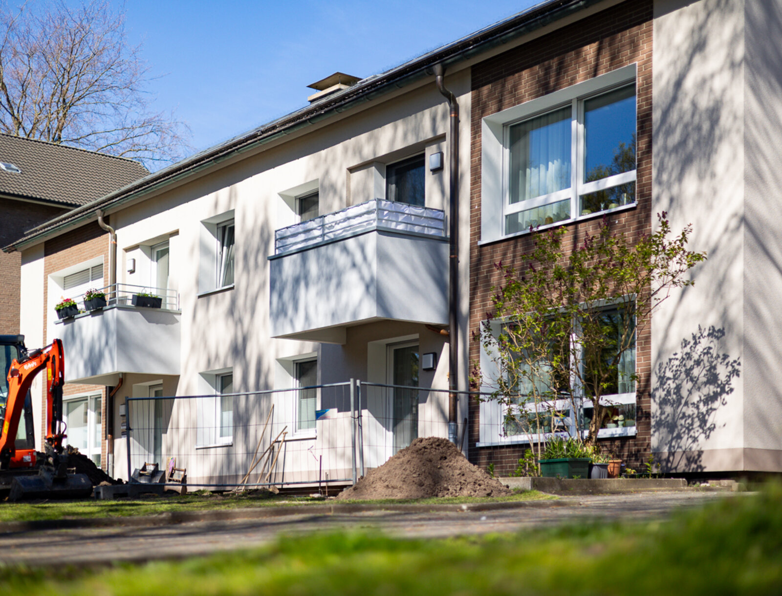 Modernisiertes Mehrfamilienhaus mit erneuerter Fassade und Balkonen. Im Vordergrund sind noch Arbeiten an den Außenanlagen im Gange.