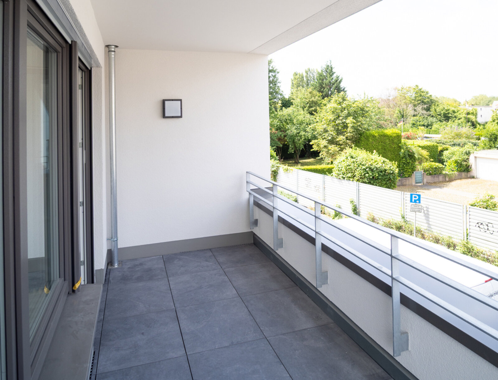 Geräumiger Balkon mit grauen Fliesen großer Fensterfront.