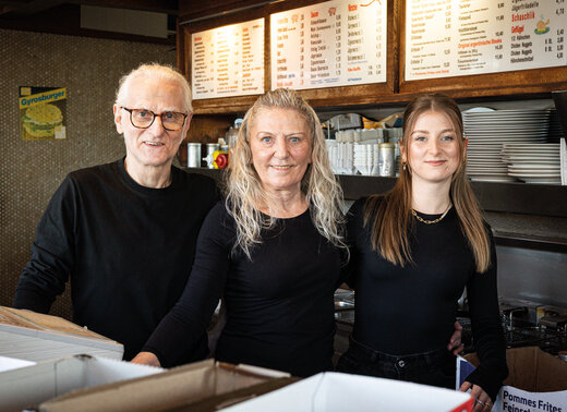 Familie Müller in der Küche ihres Imbiss. Die Personen stehen zusammen und lächeln in die Kamera.