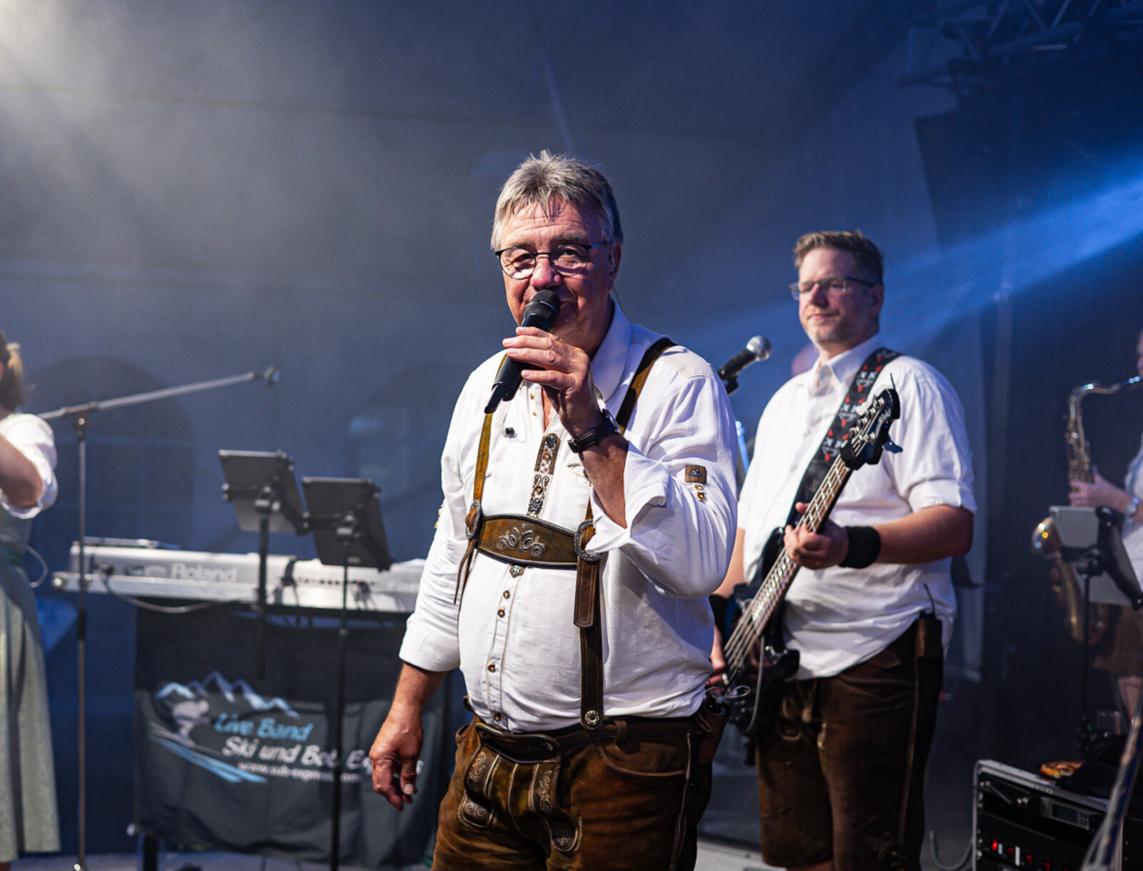 Ein Sänger steht mit Mikrofon auf der Bühne, im Hintergrund spielt die Band.