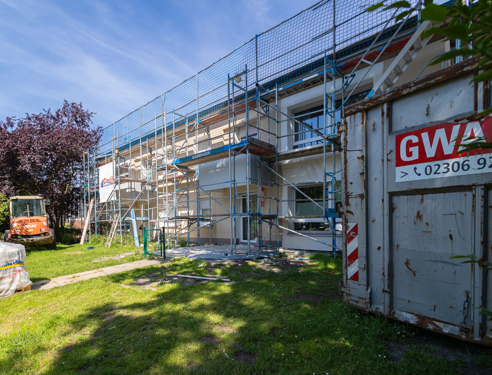 Eingerüstetes Wohngebäude während der Fassaden- und Balkonsanierung. Im Vordergrund sind ein Baucontainer und ein Baustellenfahrzeug zu sehen.