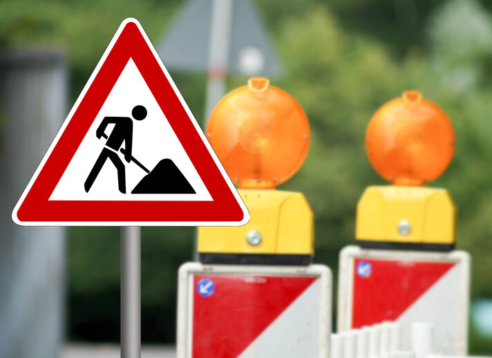 Baustellenschild und Absperrbaken mit Warnleuchten weisen auf Straßenbauarbeiten hin.