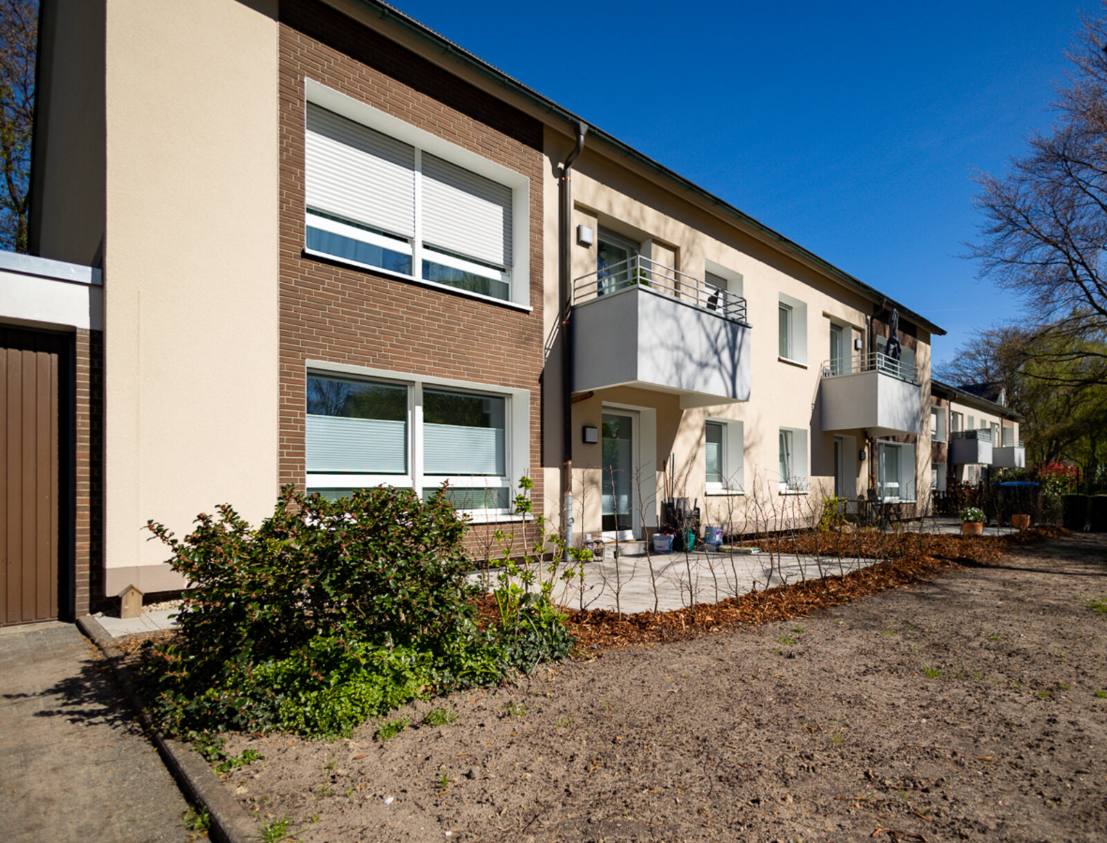 Modernisiertes Mehrfamilienhaus mit hell gestalteter Fassade, Balkonen und neu angelegten Außenflächen.