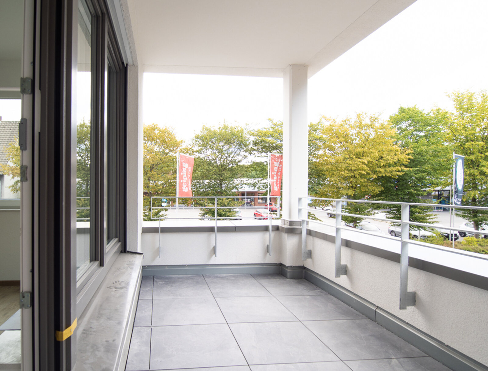 Geräumiger Balkon mit grauen Fliesen großer Fensterfront.