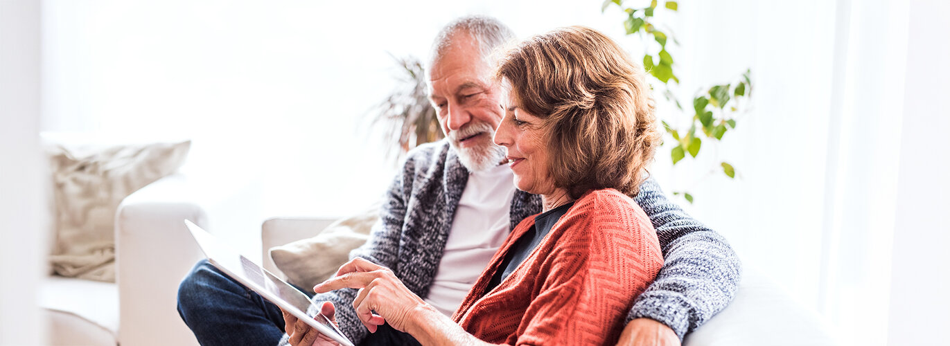 Halfpoint | Adobe Stock Ein Pärchen mittleren Alters sitzen auf dem Sofa und schauen gemeinsam auf ein Tablet.