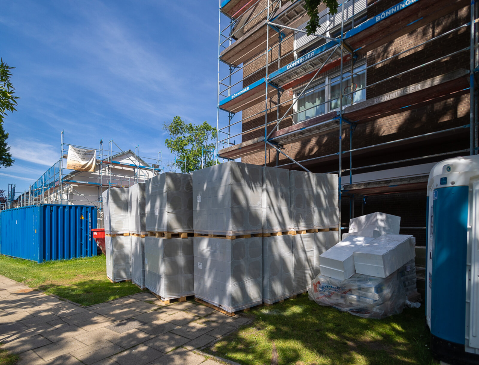 Baustellenmaterial für die Fassadendämmung lagert auf Paletten vor einem eingerüsteten Wohngebäude. Die Aufnahme dokumentiert die Vorbereitungen für die energetische Modernisierung.