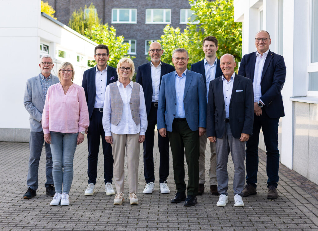 Gruppenfoto: Die Personen stehen gemeinsam vor der Verwaltung und lächeln in die Kamera.