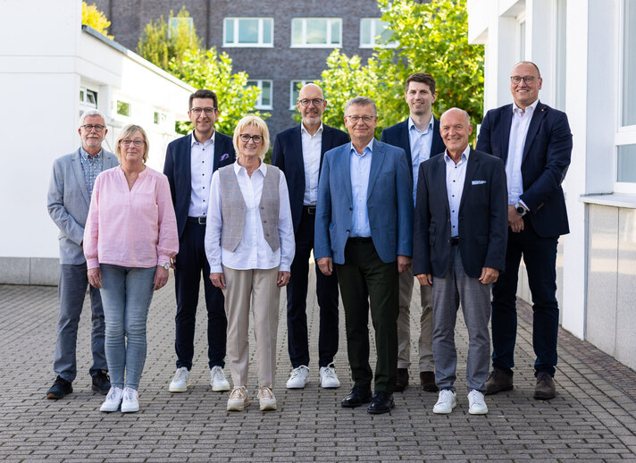 Gruppenfoto: Die Personen stehen gemeinsam vor der Verwaltung und lächeln in die Kamera.