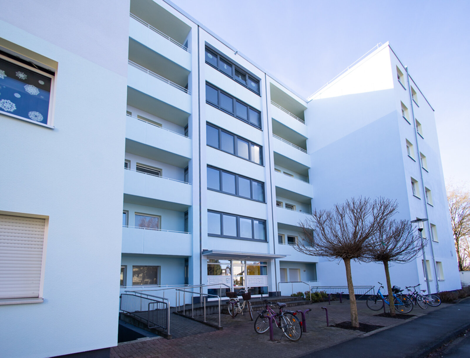 Modernisiertes Mehrfamilienhaus mit Balkonen, Fahrradstellplätzen und hellem Eingangsbereich.