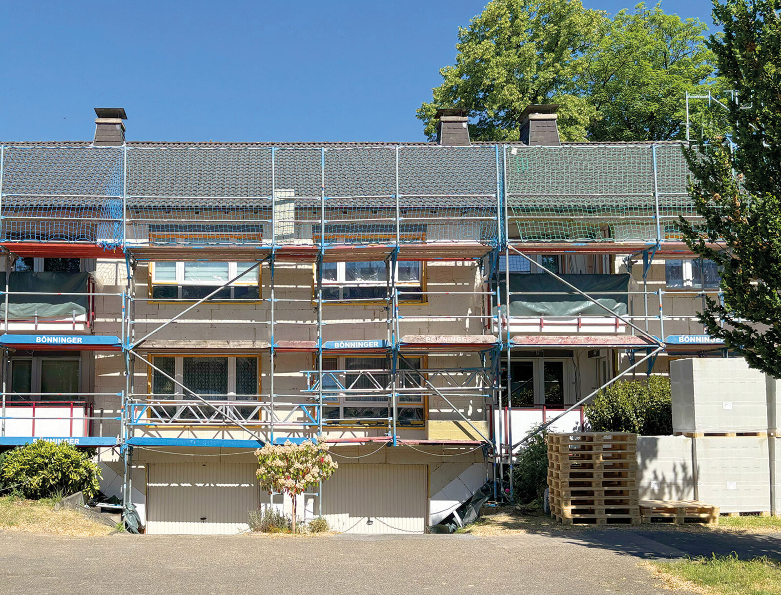 Mehrfamilienhaus während der Modernisierung mit Gerüst. Im Vordergrund liegen Baumaterialien und Paletten.
