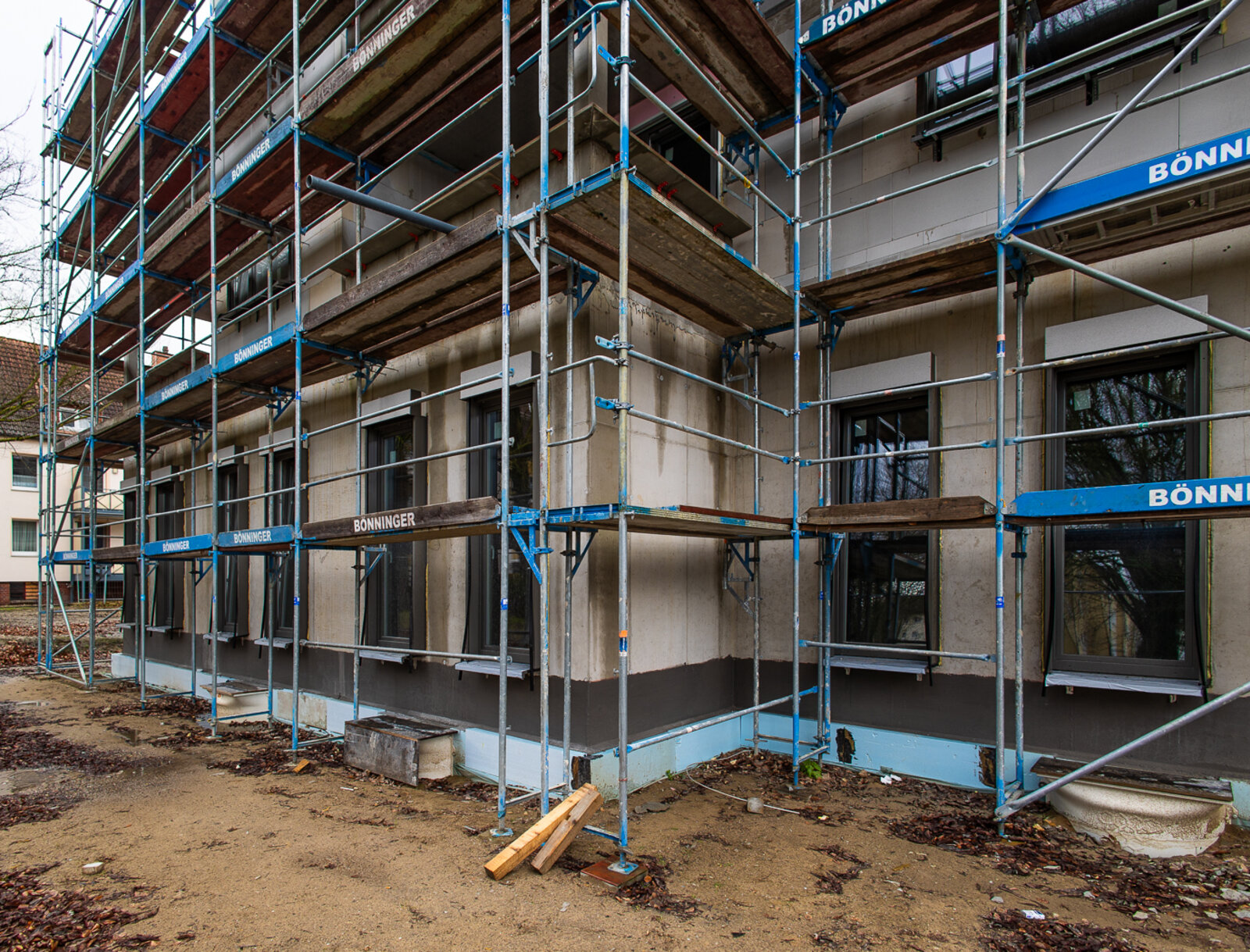 Neubau des Wohn- und Geschäftshauses in Lünen, vollständig von Baugerüst umgeben, mit Außentreppen am Gerüst und Baustellenabsperrungen im Vordergrund.