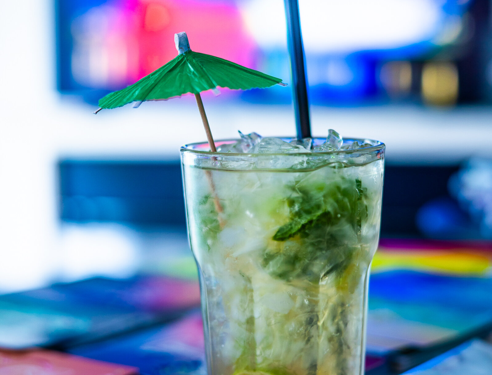 Ein alkoholfreier Cocktail mit Eis, Limette und Minze steht auf einem Tisch. Ein kleiner Papierschirm schmückt das Getränk.