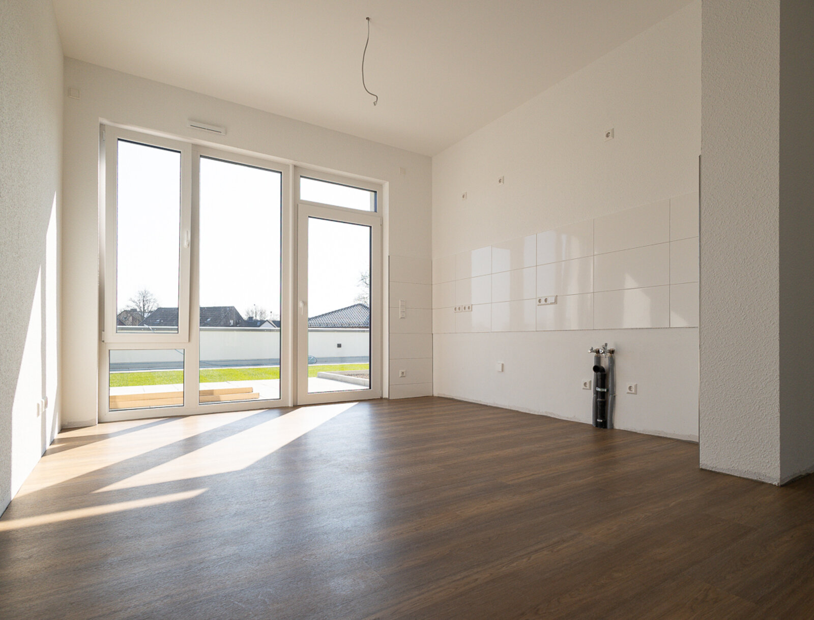 Heller Küchenbereich einer Neubauwohnung mit offener Küchenzeile, bodentiefen Fenstern und Außenzugang.