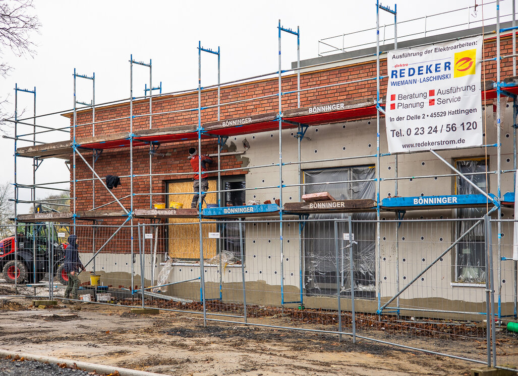 Mitarbeitende des Bauunternehmens stehen auf einem Gerüst und bringen Klinkerriemchen an die Fassade an