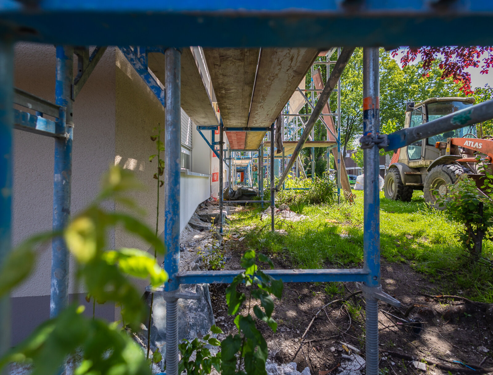 Blick unter das Fassadengerüst eines Mehrfamilienhauses während der Modernisierungsarbeiten. Gerüst, Baustellenfahrzeug und freigelegte Arbeitsbereiche zeigen den laufenden Baufortschritt.