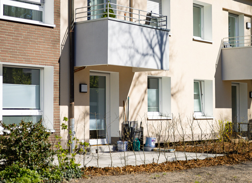 Detailansicht eines modernisierten Mehrfamilienhauses mit neuem Balkon, heller Fassade und frisch angelegten Außenflächen.