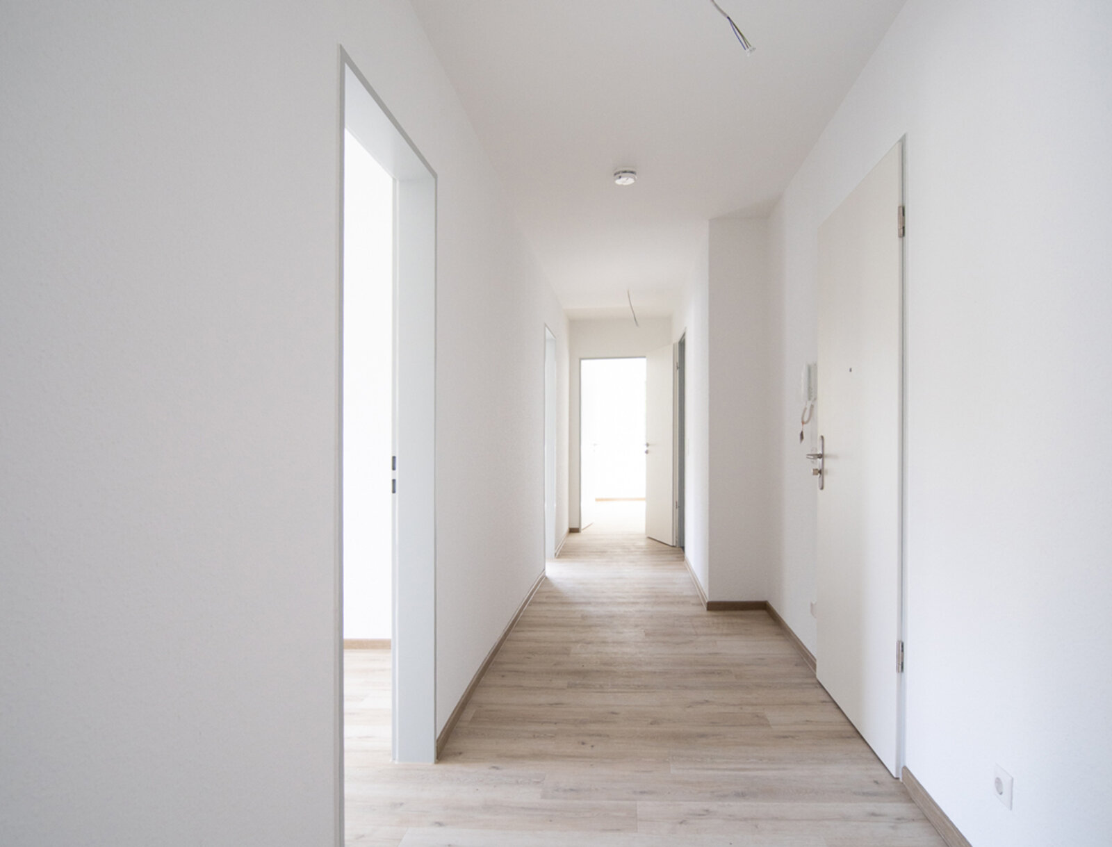 Blick in den Flur einer Neubauwohnung. Ausstattung mit hellem Laminat und weißer Raufasertapete.