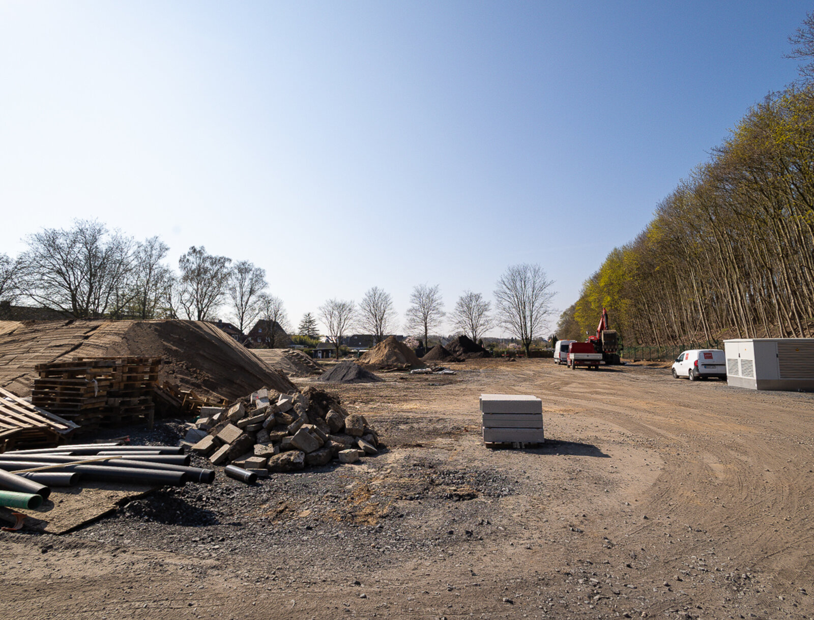 Erschlossene Baufläche mit Baumaterialien, Erdaufschüttungen und Baufahrzeugen auf dem zukünftigen Baufeld.