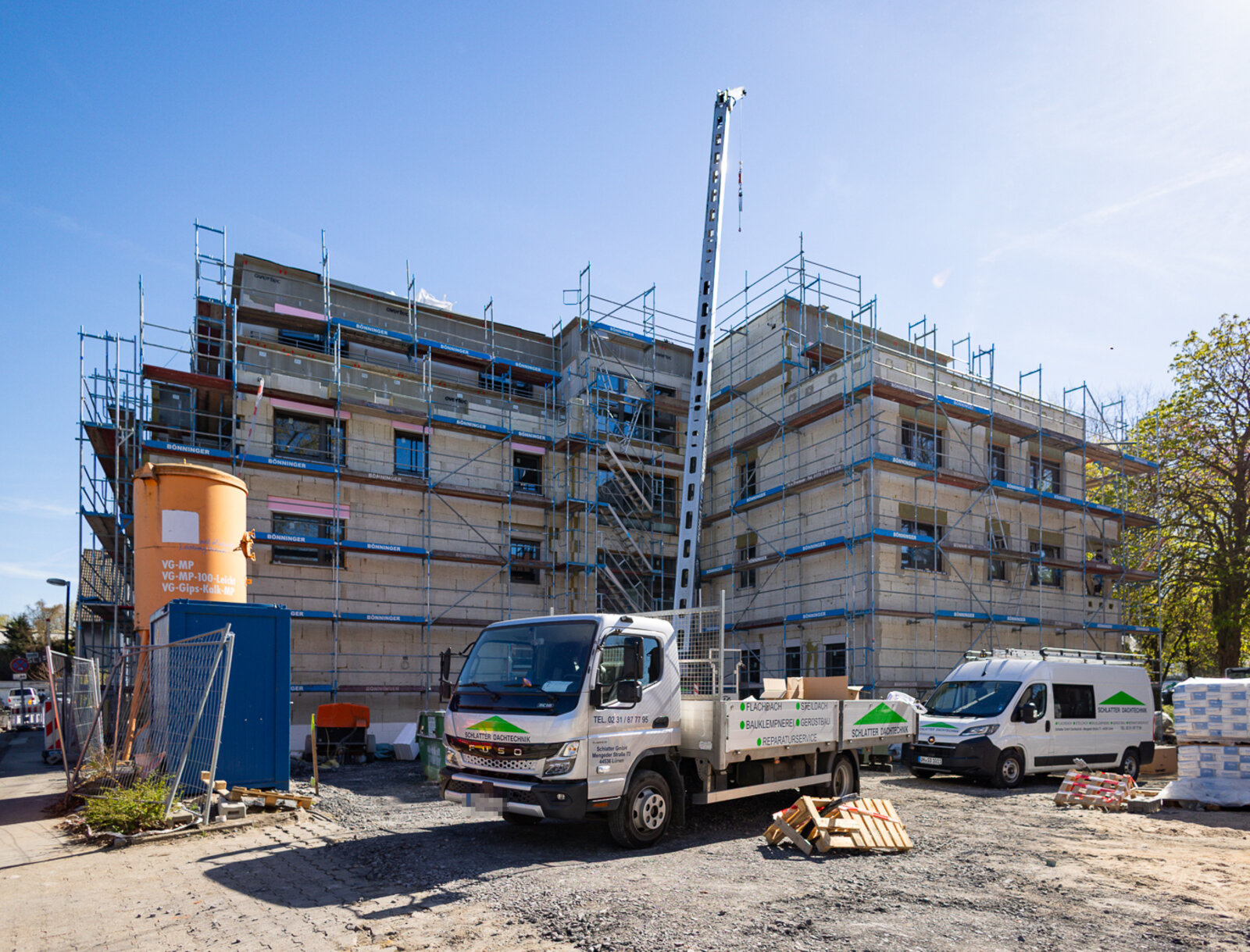 Eingerüstetes Gebäude mit Baustellenfahrzeugen und Materialien auf dem Gelände.