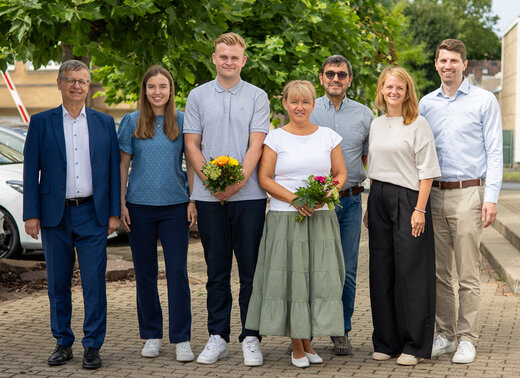 Gruppenfoto: Die Personen stehen gemeinsam vor der Verwaltung und lächeln in die Kamera.