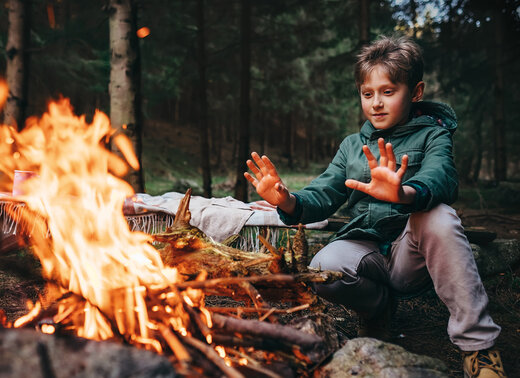 Junge wärmt seine Hände an einem Lagerfeuer im Wald.