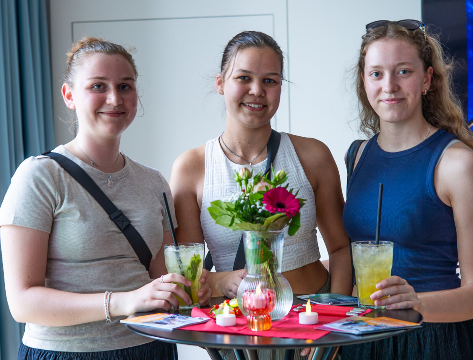 Drei Besucherinnen der Lüner Nacht der Ausbildung stehen mit Cocktails an einem Stehtisch und lächeln freundlich in die Kamera.